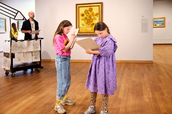 Twee meisjes zijn aan het tekenen voor het schilderij Zonnebloemen van Van Gogh in het Van Gogh Museum. Naast het schilderij staat de Tekenkar. foto: Suzanne Karsters